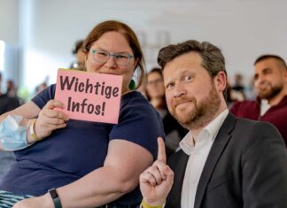 Eine Frau hält eine rosafarbenen Zettel hoch mit der Aufschrift „Wichtige Infos!“. Daneben ein Mann, der leicht skeptisch-fordernd darauf zeigt.